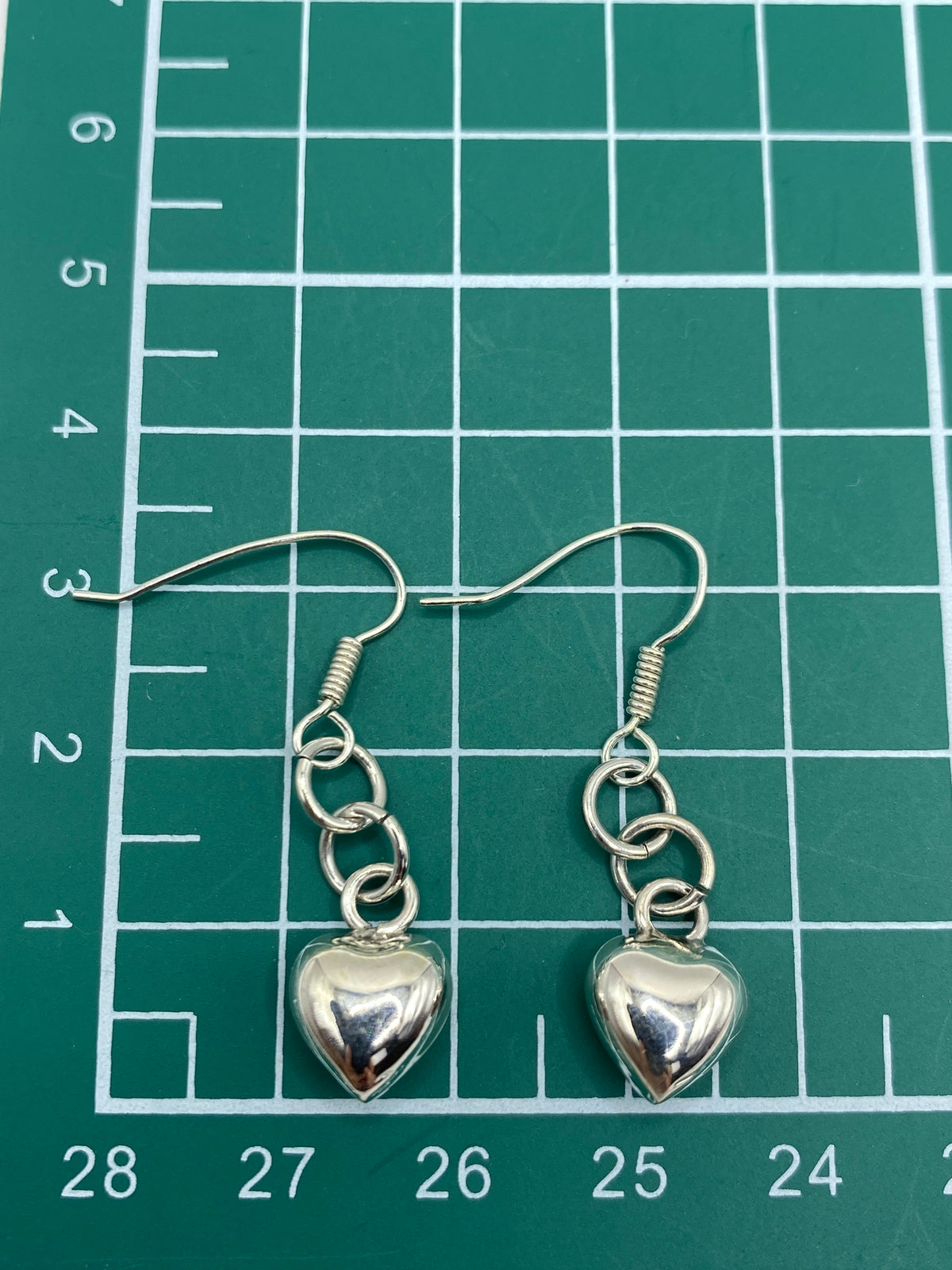 Aretes de plata corazón cartoneado sostenidos en la mano mostrando tamaño real