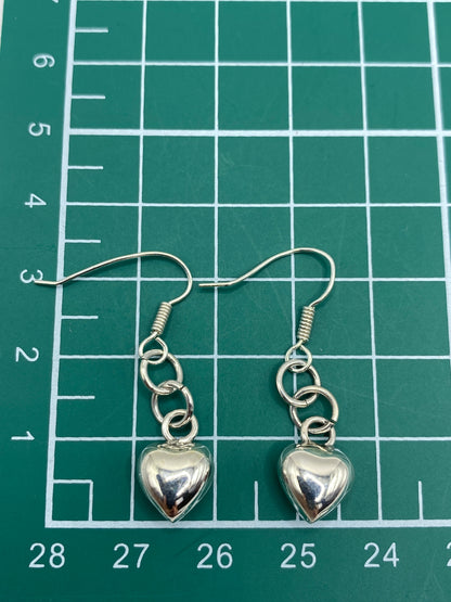 Aretes de plata corazón cartoneado sostenidos en la mano mostrando tamaño real