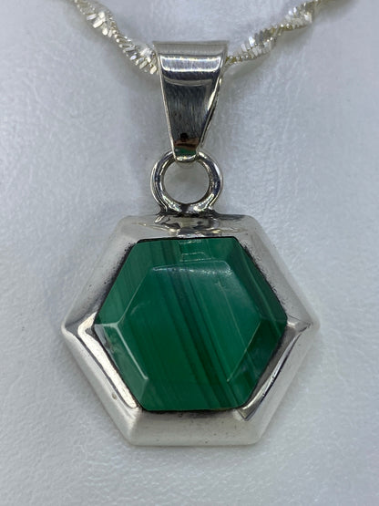 Dije hexagonal de plata 925 con piedra verde engastada a mano, colgando de cadena plateada