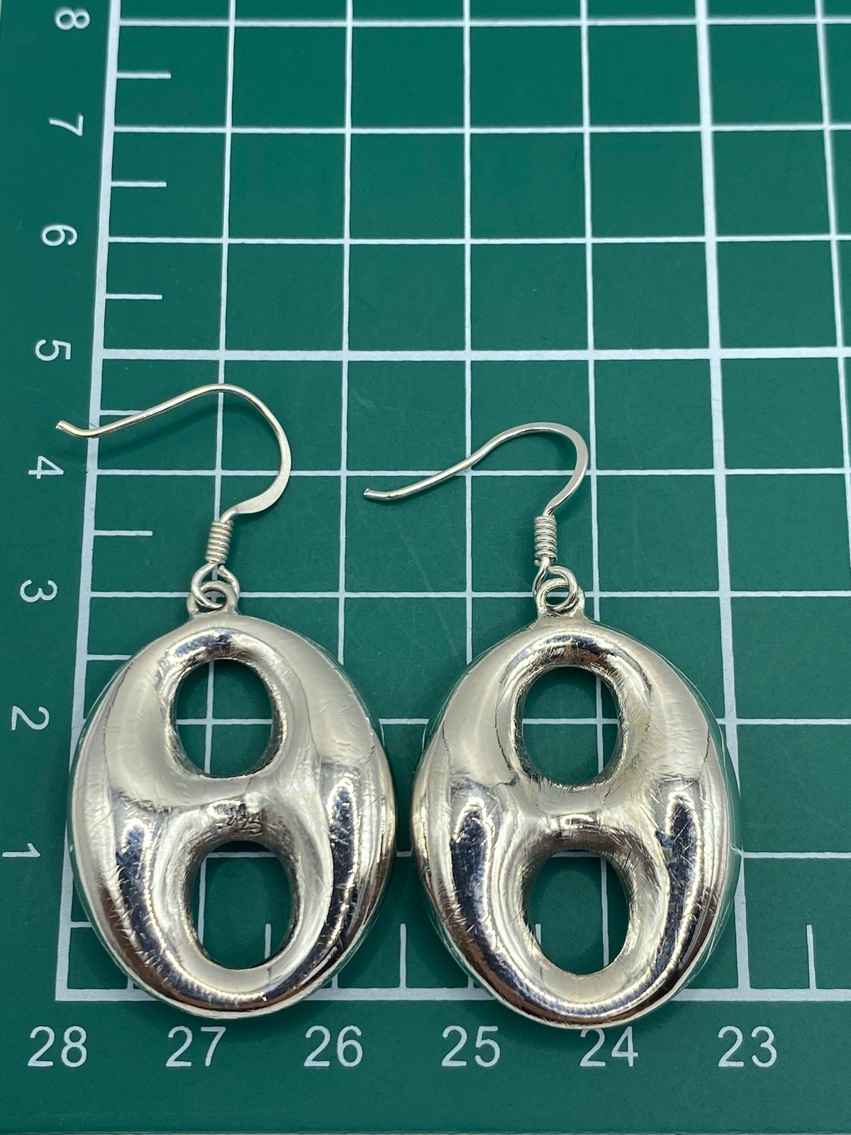 Los aretes sobre regla mostrando largo de 4.7 cm y Quinto 925 de autenticidad
