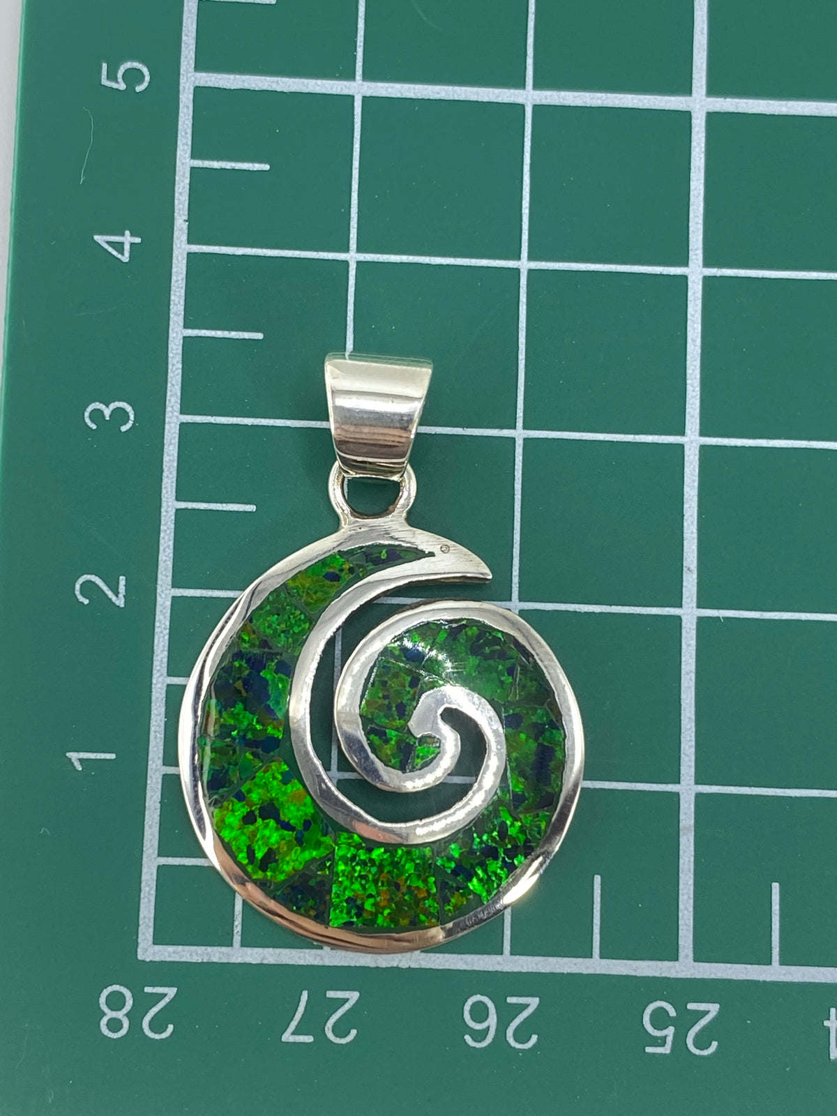 Dije espiral con ópalo verde sostenido en una mano, mostrando el tamaño de 3.4 cm