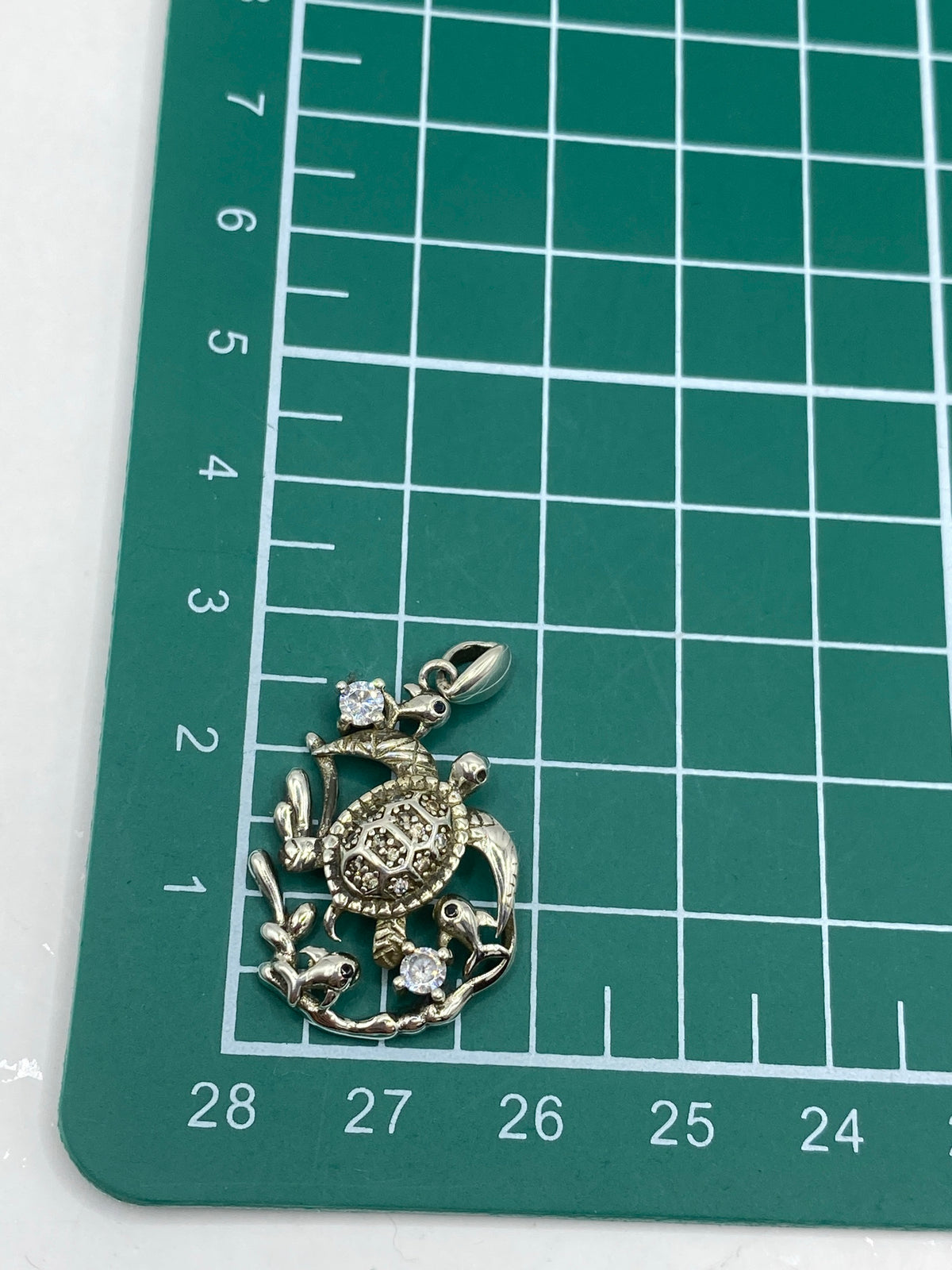 Medición del dije en escala: 3 cm de largo × 2 cm de ancho, con pesa de 3.27 g