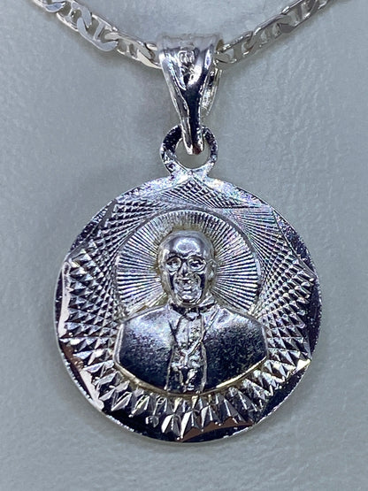 Dije de plata repujado con figura religiosa y halo radiante, frente al pecho