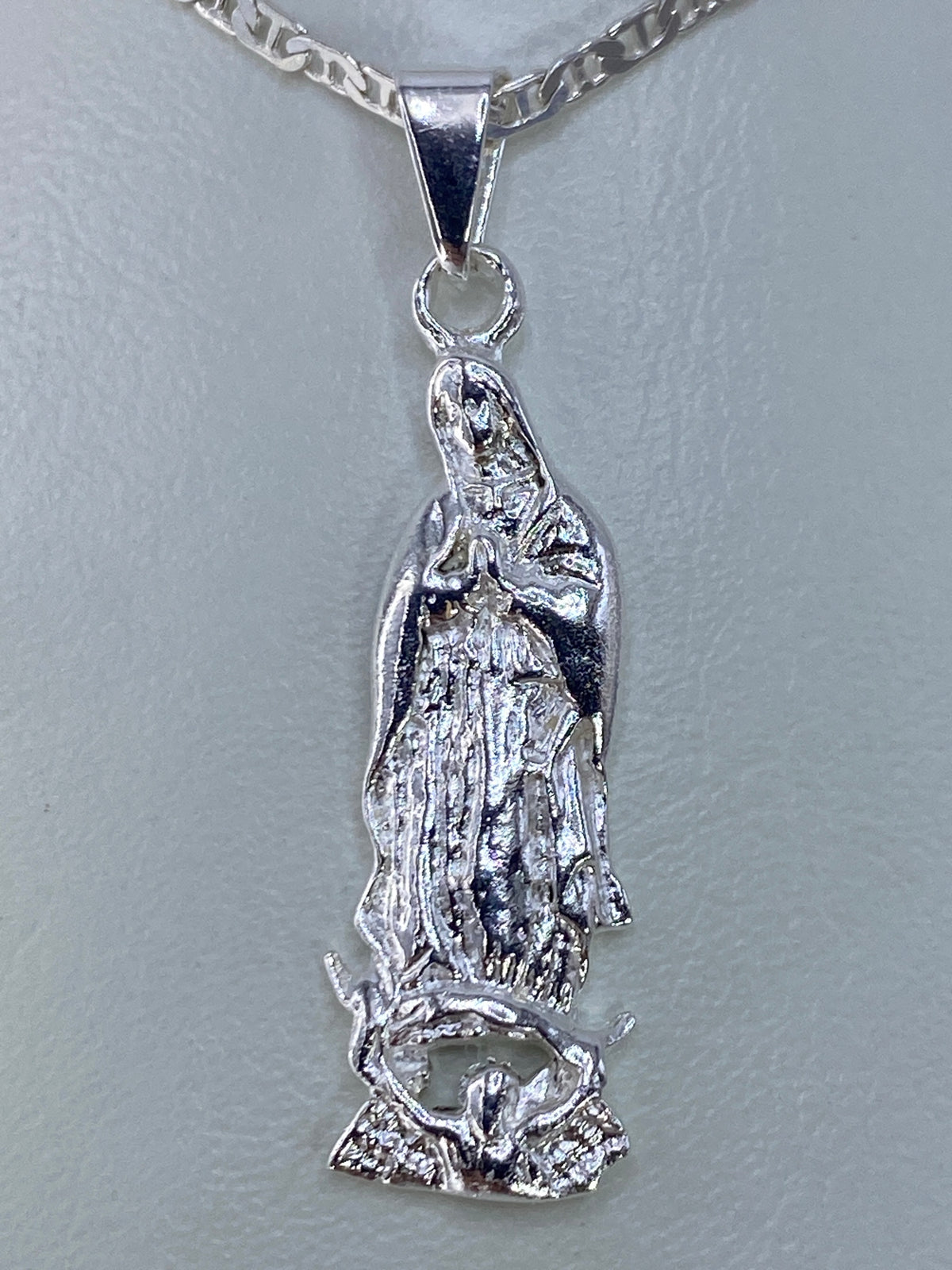 Dije de plata repujada con imagen de la Virgen María, 4 cm de largo, colgado de una cadena plateada
