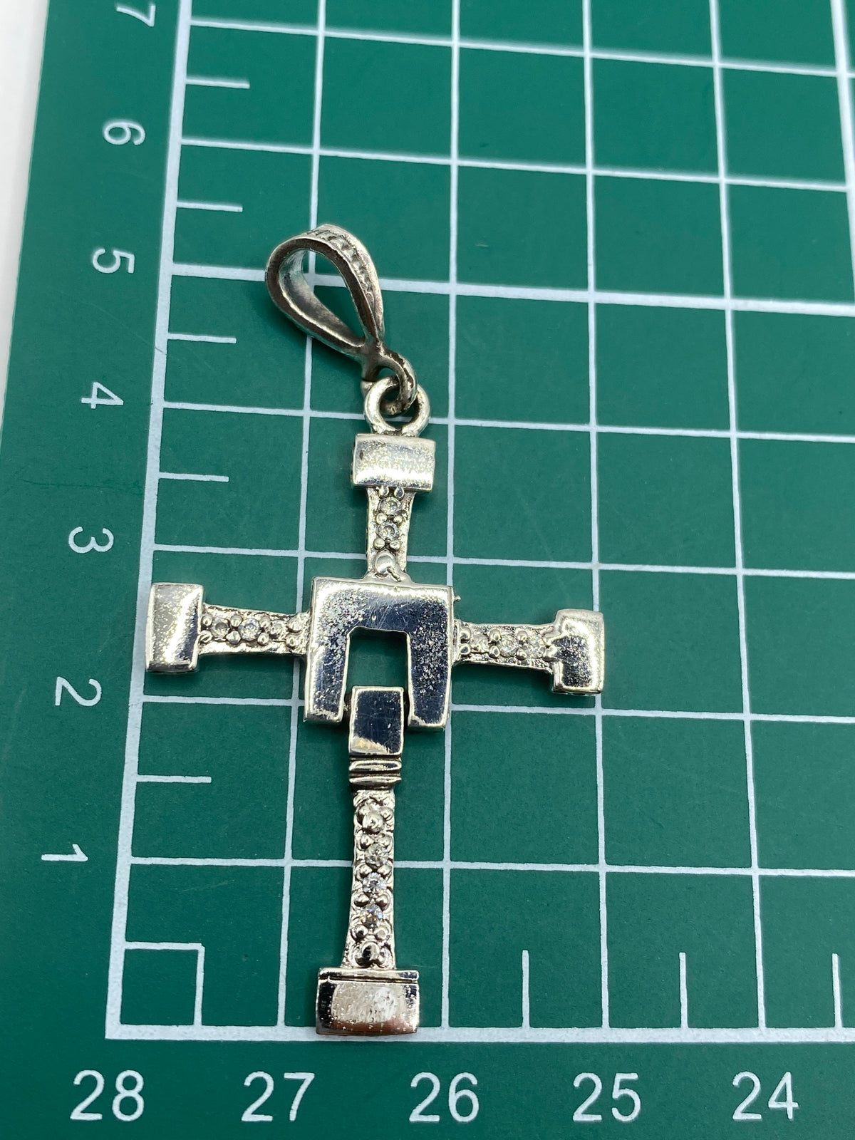 Cruz sobre regla mostrando medidas de 5.5 cm de largo × 3 cm de ancho
