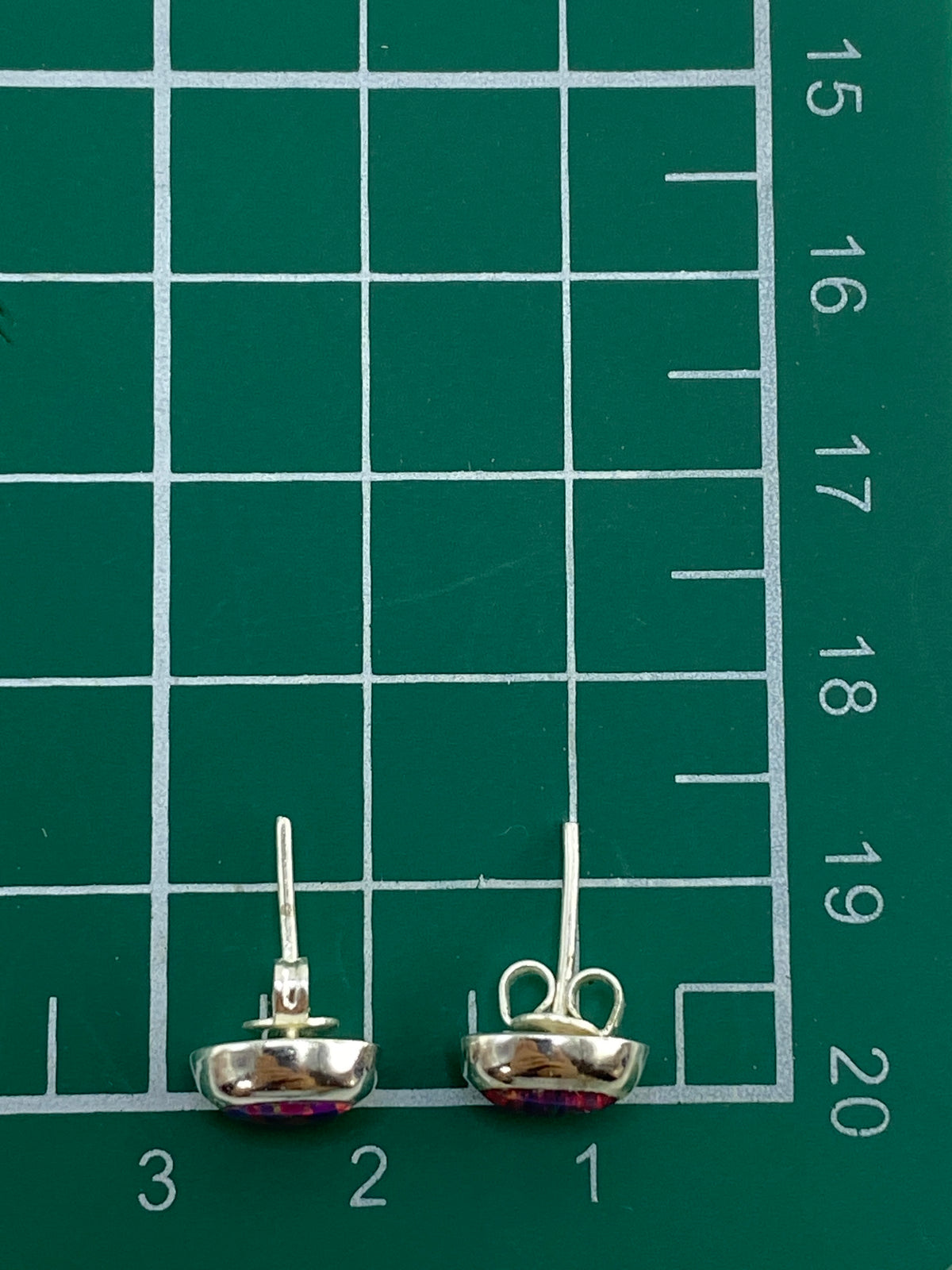 Aretes de plata con ópalo rosa sobre fondo blanco con escala de medida