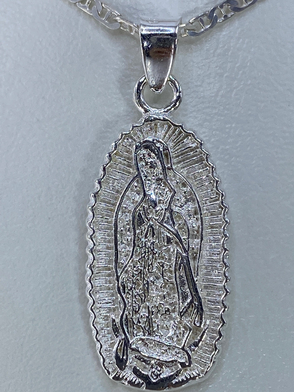 Dije de la Virgen de Guadalupe sobre papel métrico mostrando su tamaño de 3.5 cm