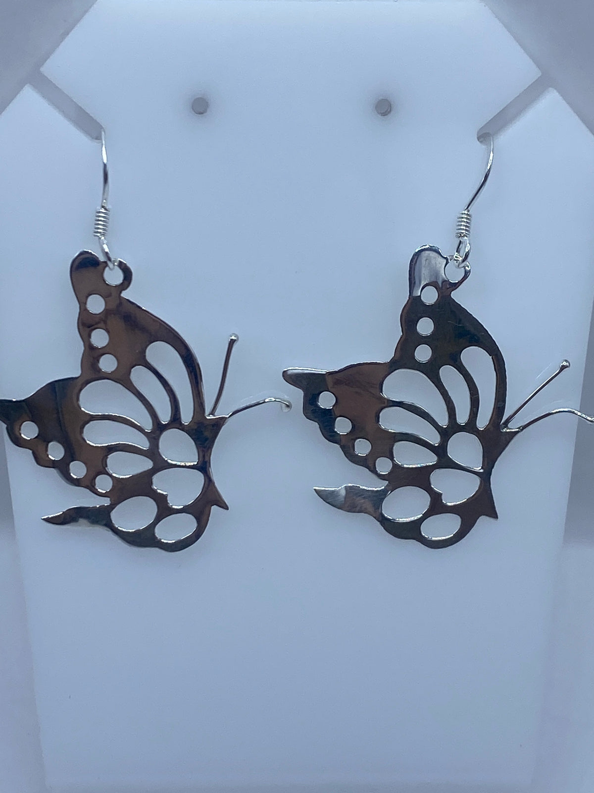Aretes mariposa de plata sobre escalímetro verde, mostrando las medidas reales de 5.5 cm