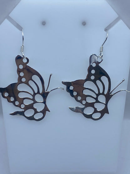 Aretes mariposa de plata sobre escalímetro verde, mostrando las medidas reales de 5.5 cm