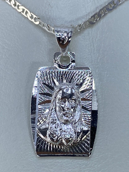 Dije de plata repujado con rostro religioso y rayos de devoción, sobre cadena de eslabón