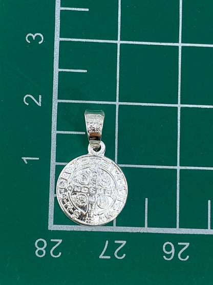 Medalla de San Benito de 1.9 cm sobre fondo gris, escala visible