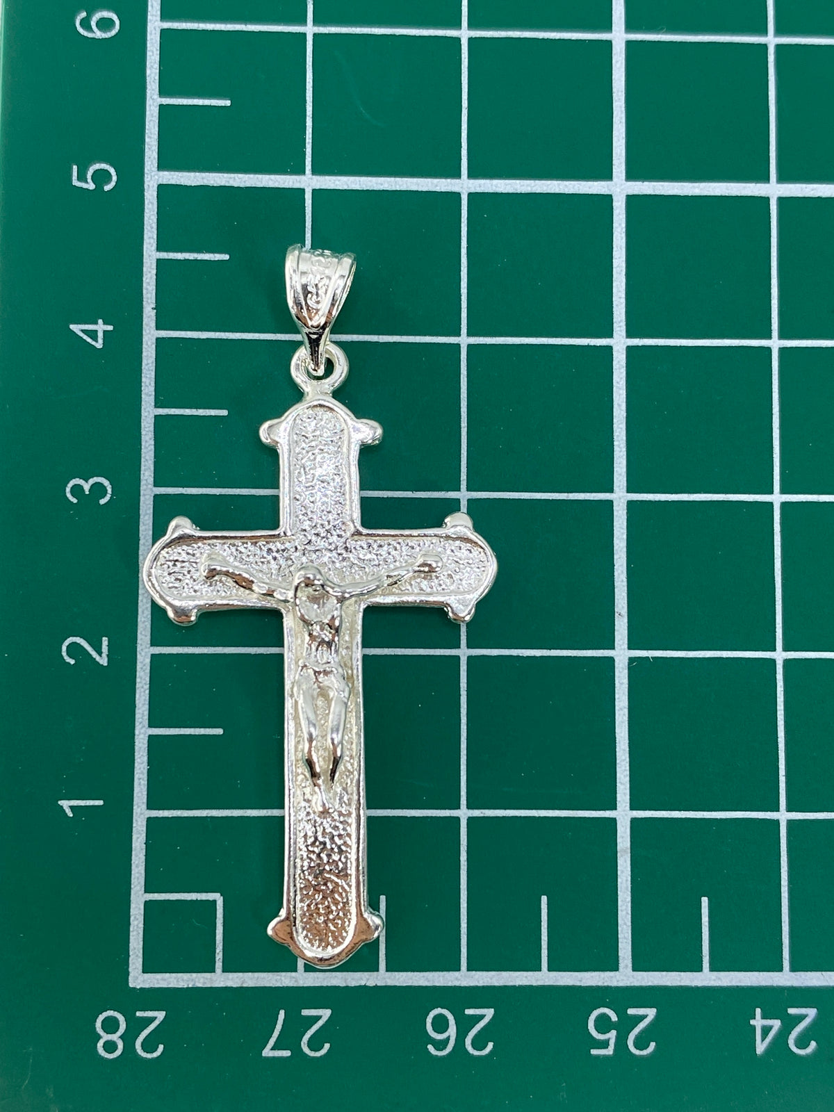 Comparación de tamaño del dije: crucifijo de 4.5 cm junto a medida de escala