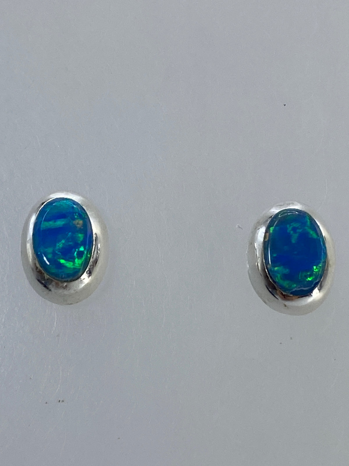 Par de aretes de plata con ópalo de fuego multicolor, vista frontal sobre fondo blanco