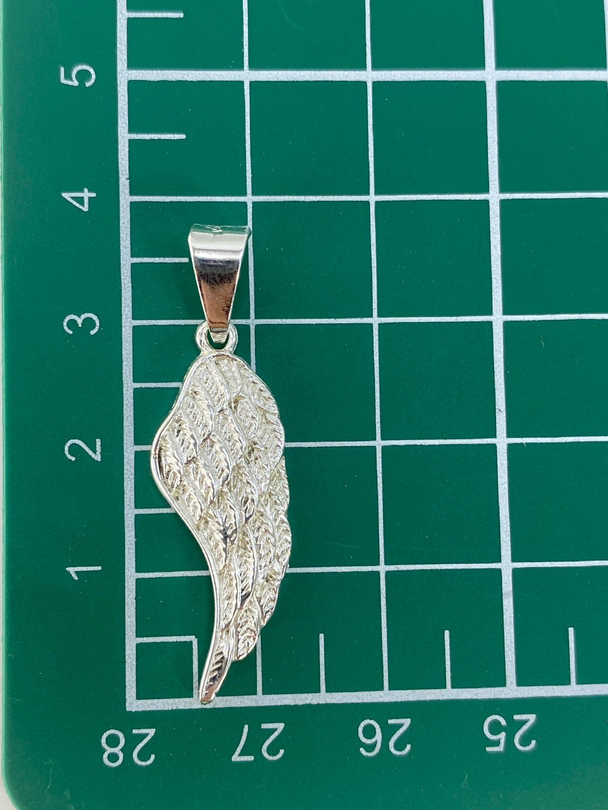 Ala de plata sobre escala de medición, confirmando 3.8 cm de largo