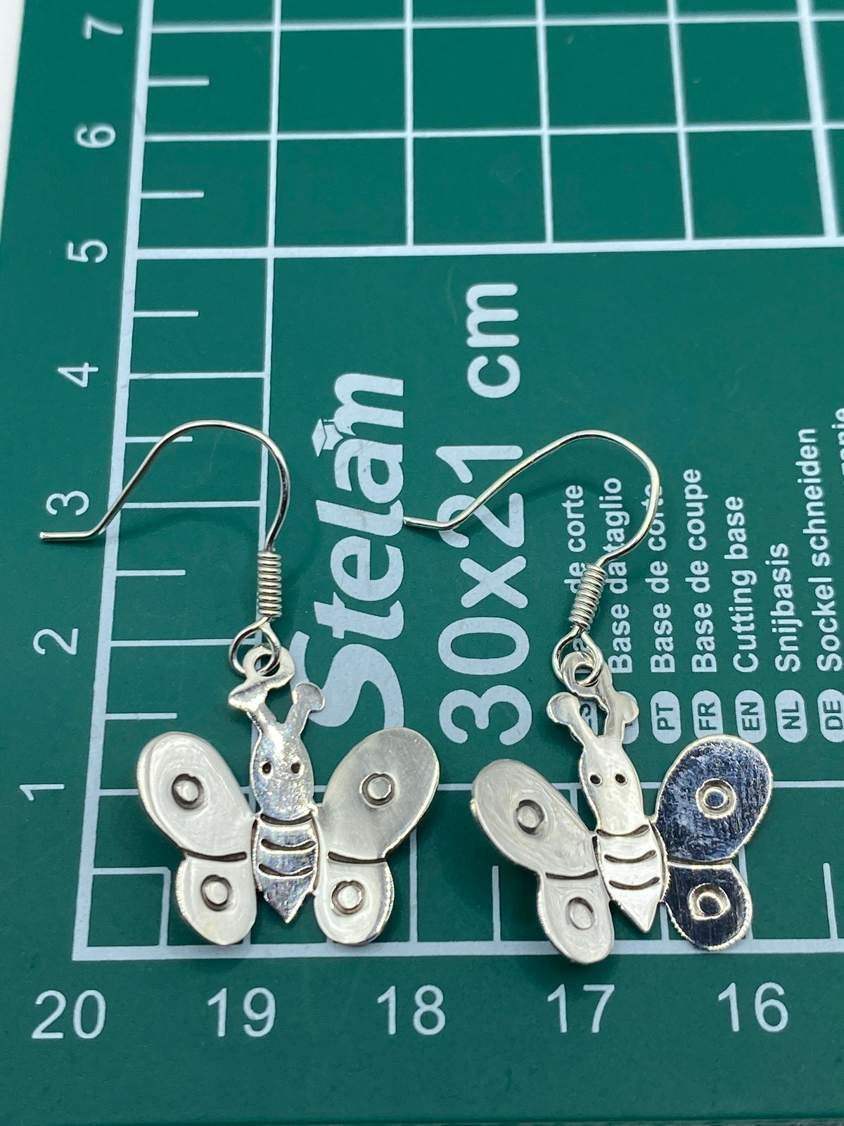 Ambos aretes de plata mariposa sobre fondo blanco, con el Quinto grabado visible