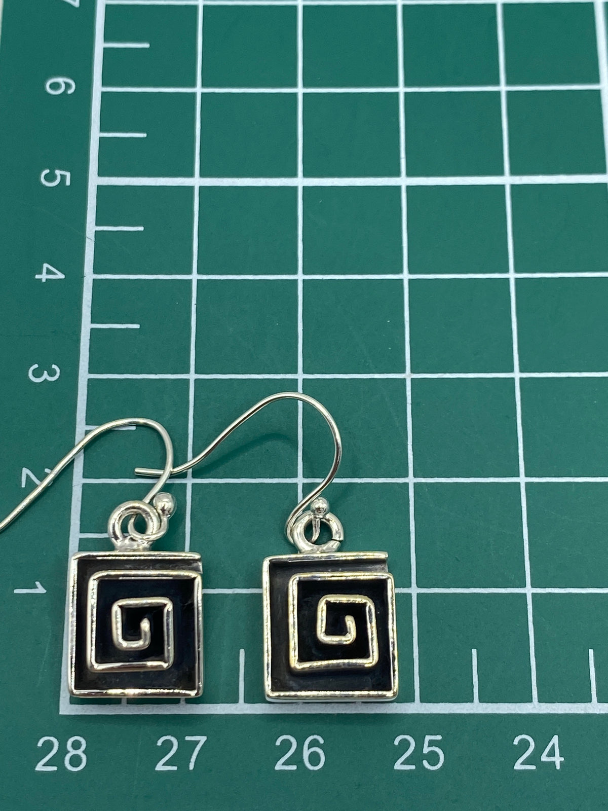 Aretes de espiral griega en plata 925 sobre fondo blanco mostrando el Quinto