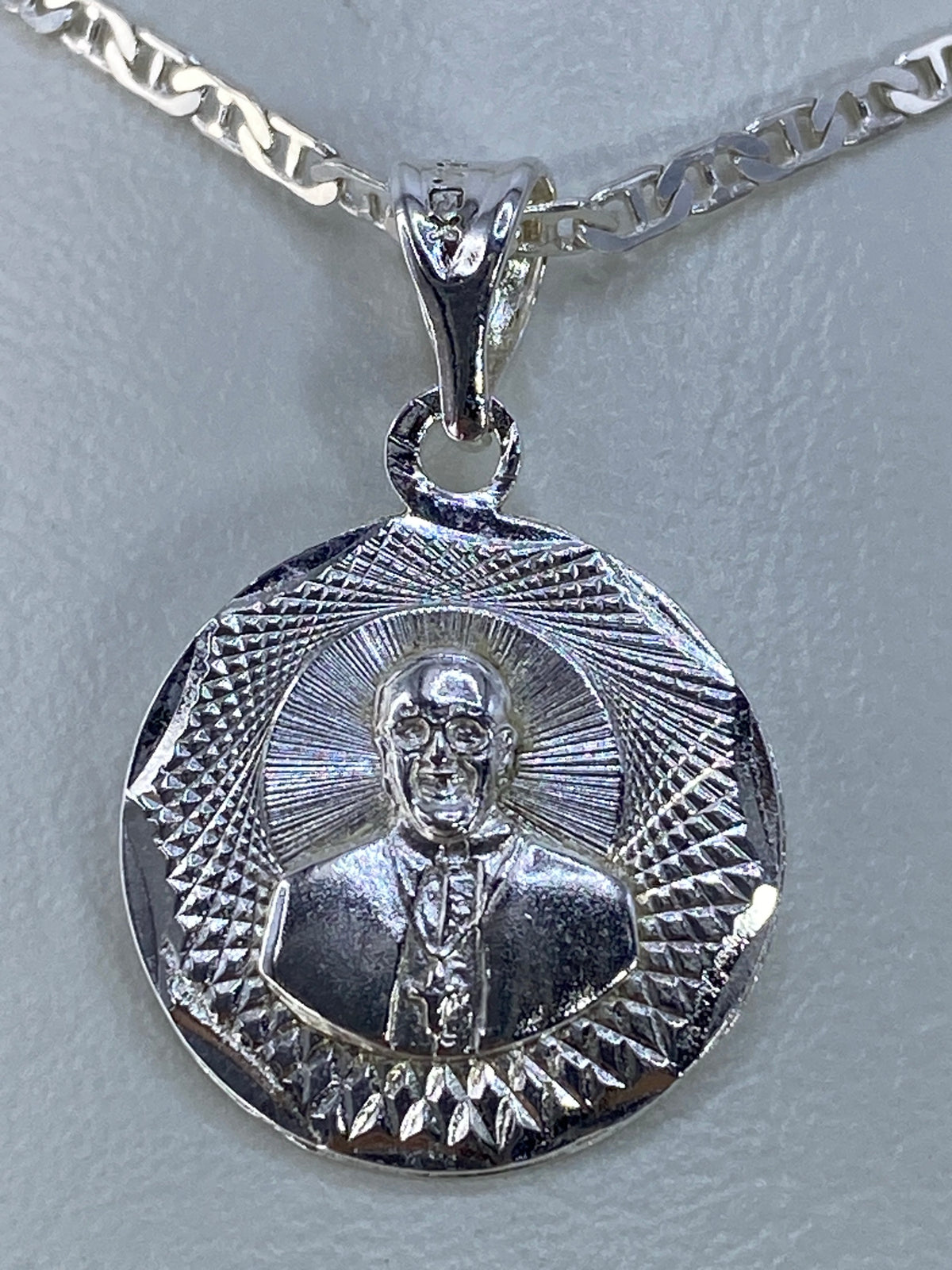 Dije de plata repujado con motivo espiritual y halo de rayos, de frente