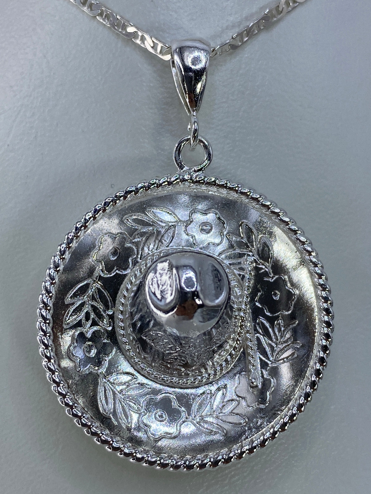 Dije de plata repujado con motivo floral en relieve, colgado de cadena plateada