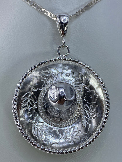 Dije de plata repujado con motivo floral en relieve, colgado de cadena plateada