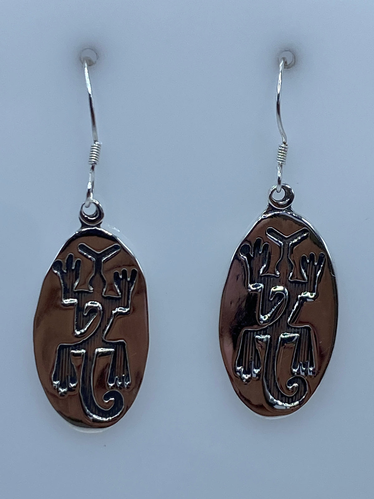 Aretes de plata repujados con motivos prehispánicos colgando del gancho