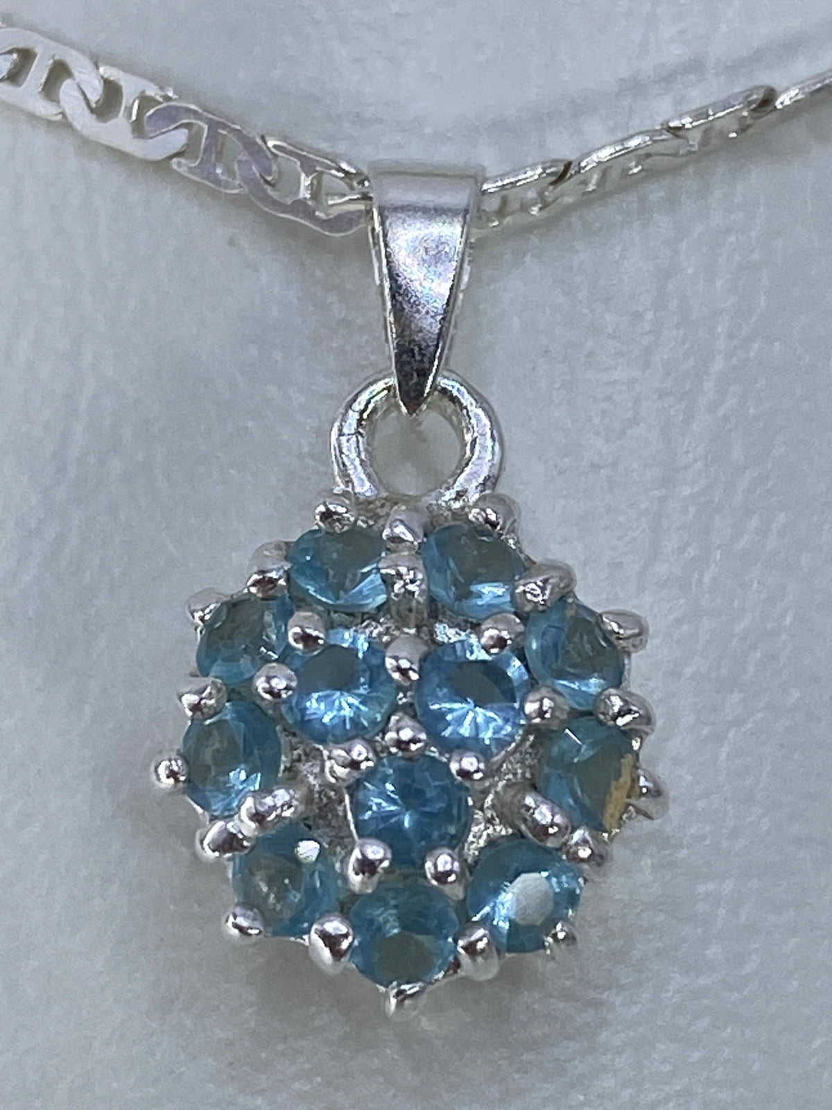 Dije de plata 925 con circonia azul cielo engastada, frente y reverso con detalle del engaste a mano