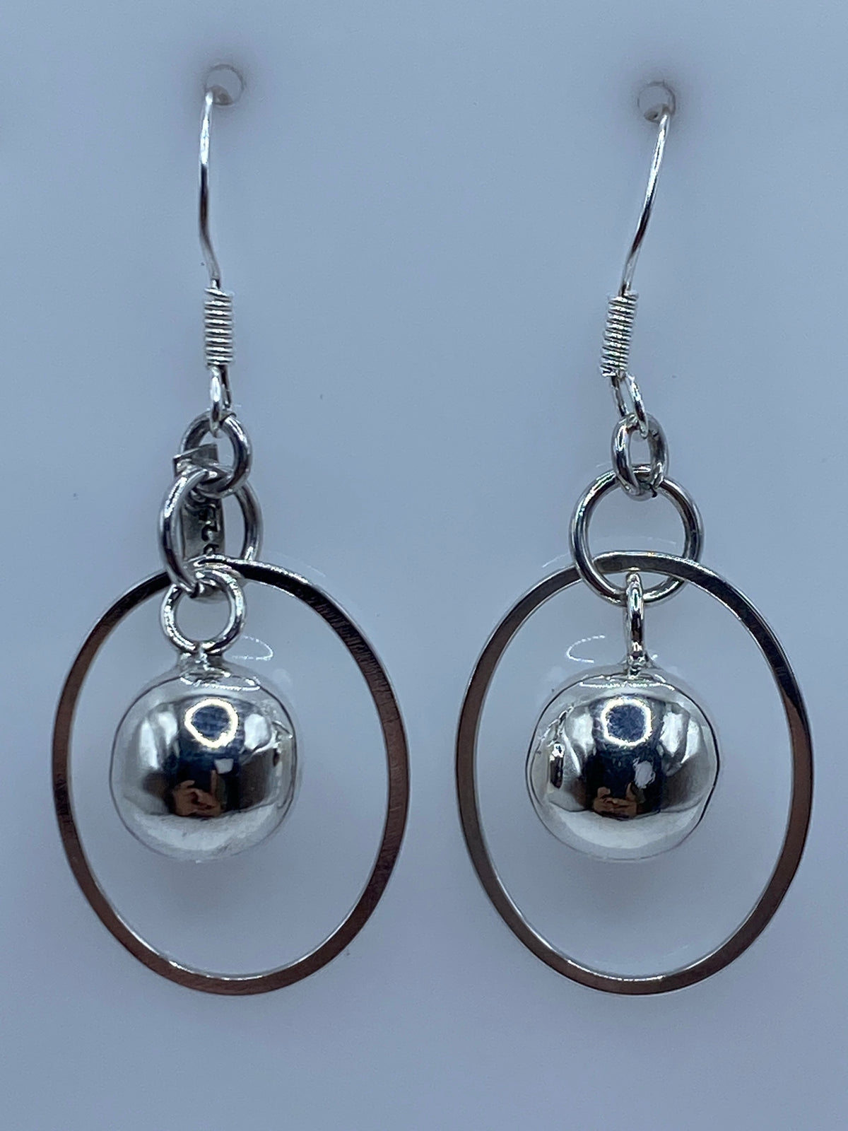 Par de aretes de plata con bola pulida y aro oval abierto, colgando lado a lado