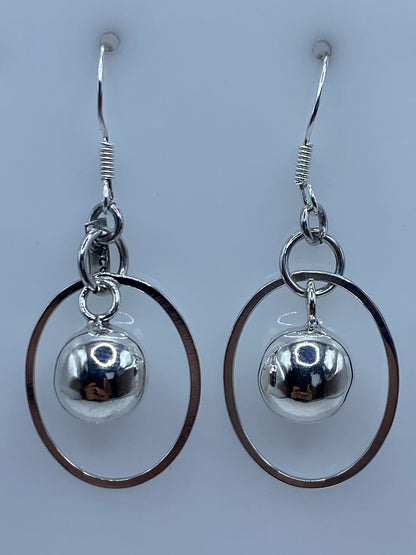 Par de aretes de plata con bola pulida y aro oval abierto, colgando lado a lado