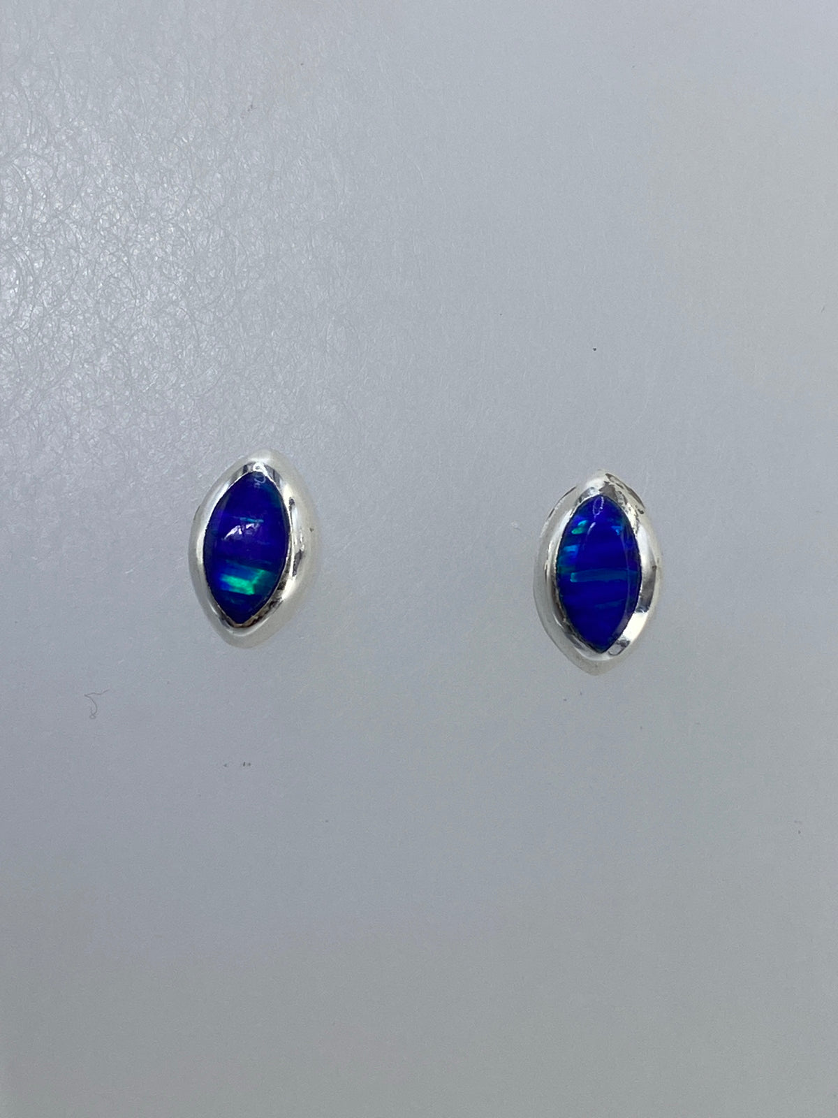 Detalle frontal de un arete mostrando el ópalo multicolor en engaste de plata