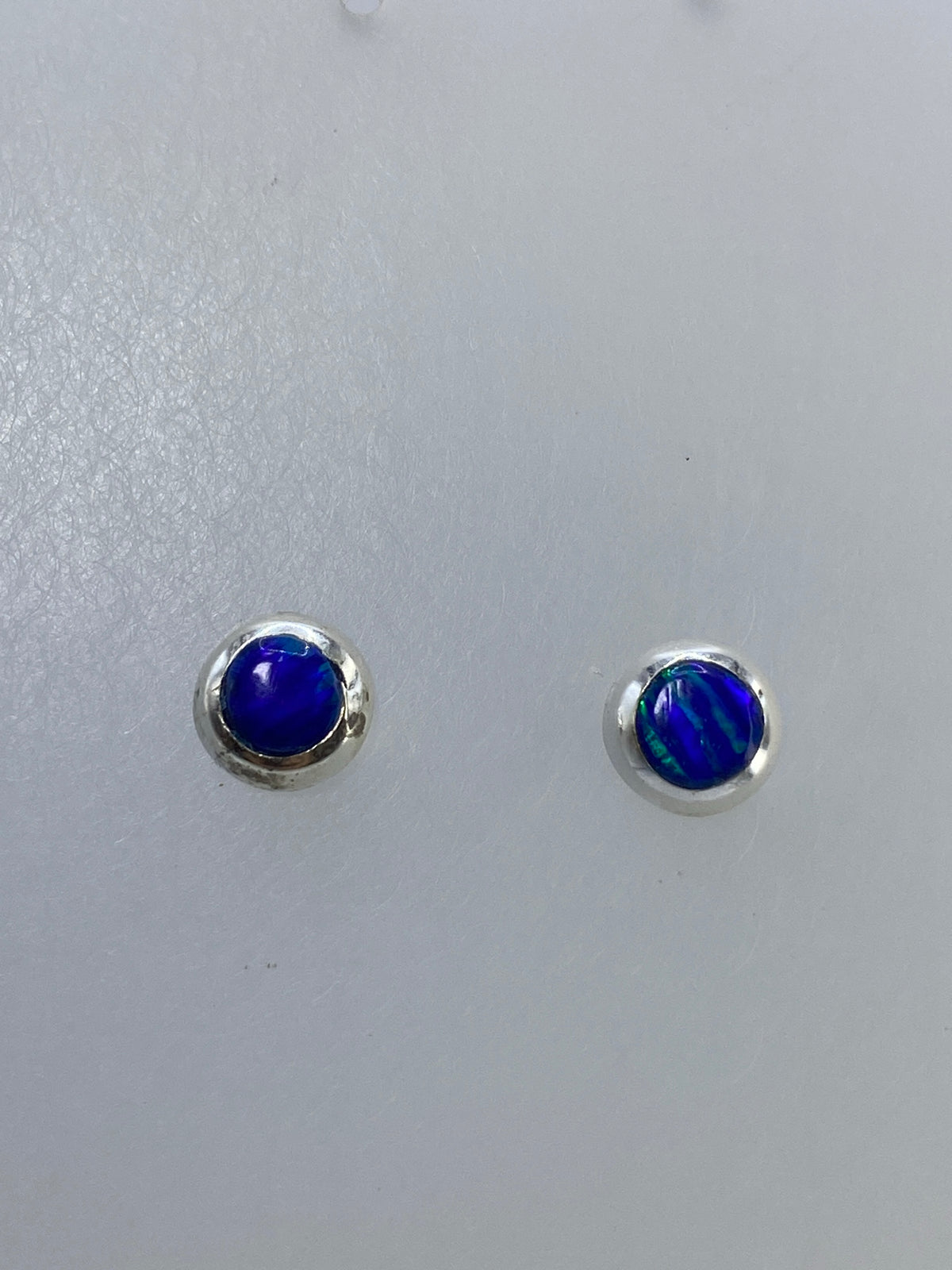 Detalle frontal de los aretes mostrando los reflejos naranjas y dorados del ópalo