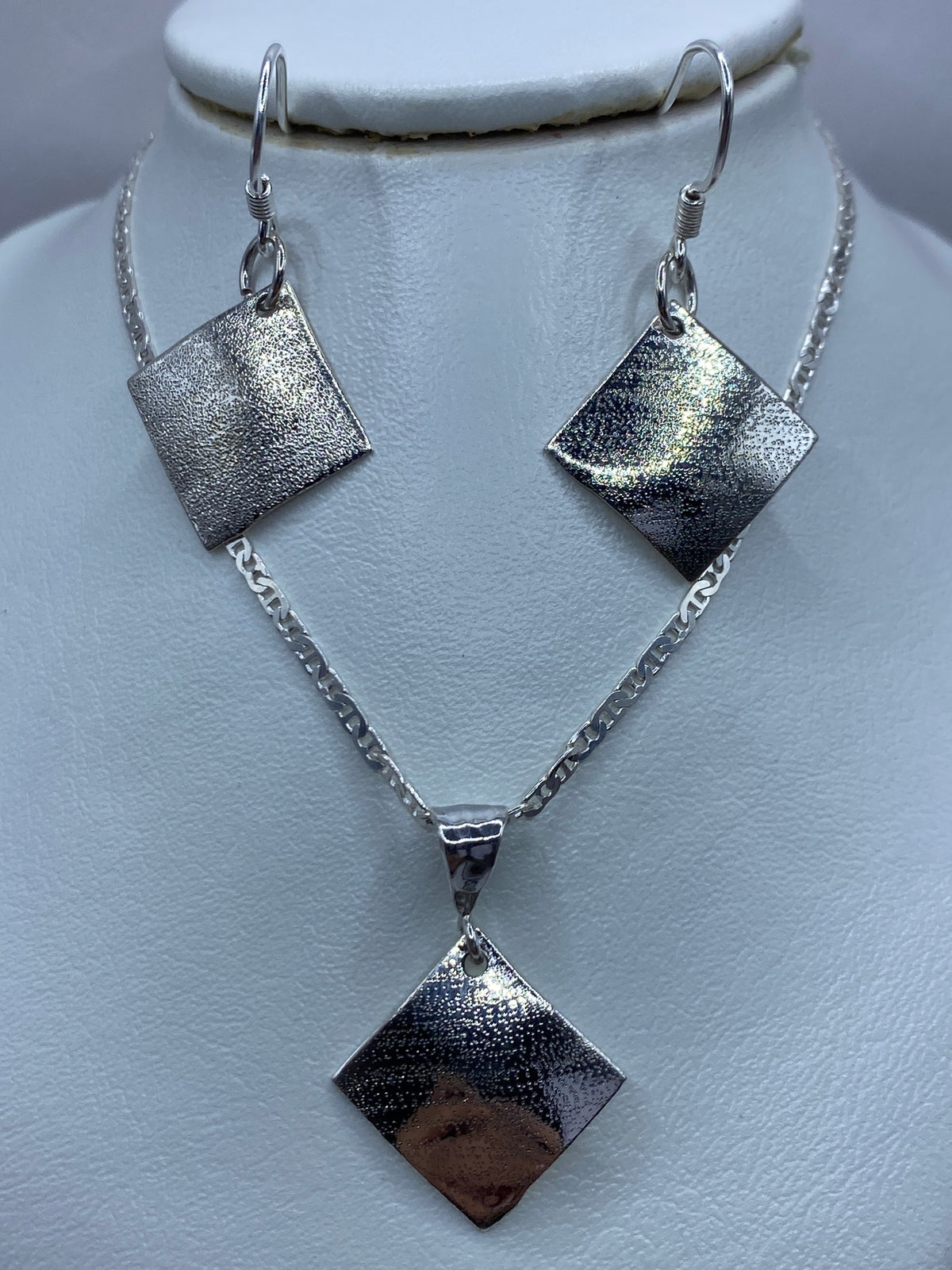 Par de aretes de plata 925 repujada cuadrados con textura martillada, colgando en display blanco