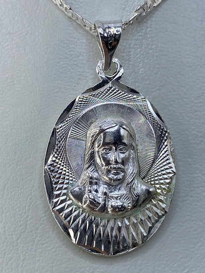 Dije de plata repujado con motivo religioso de 3.5 cm, colgando de cadena plateada