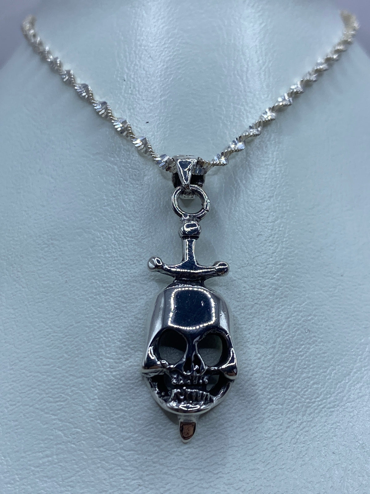 Detalle frontal del dije calavera con espada de plata, mostrando el acabado pulido