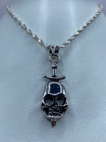 Detalle frontal del dije calavera con espada de plata, mostrando el acabado pulido