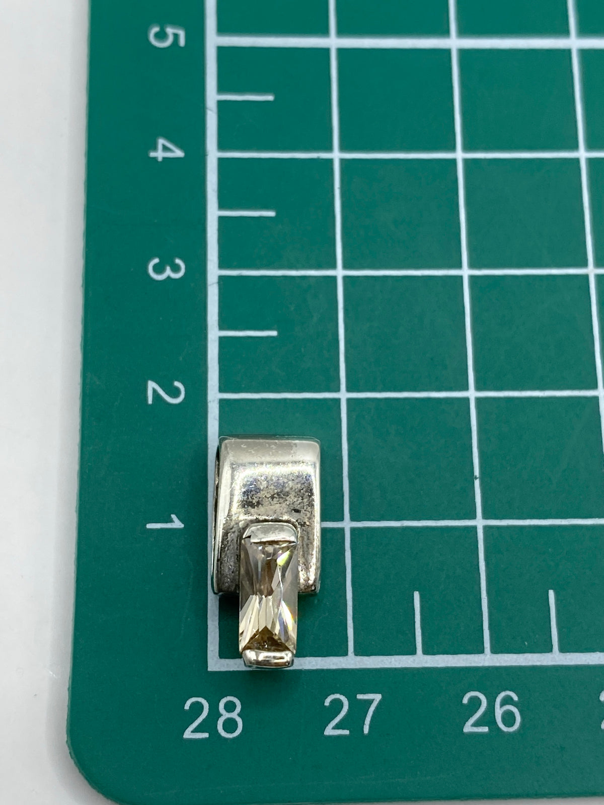 Dije de plata sobre una regla mostrando el tamaño real de 1.6 cm × 8 mm