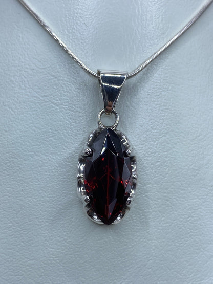 Dije de plata con circonia roja engastada, colgando de cadena de plata, vista frontal