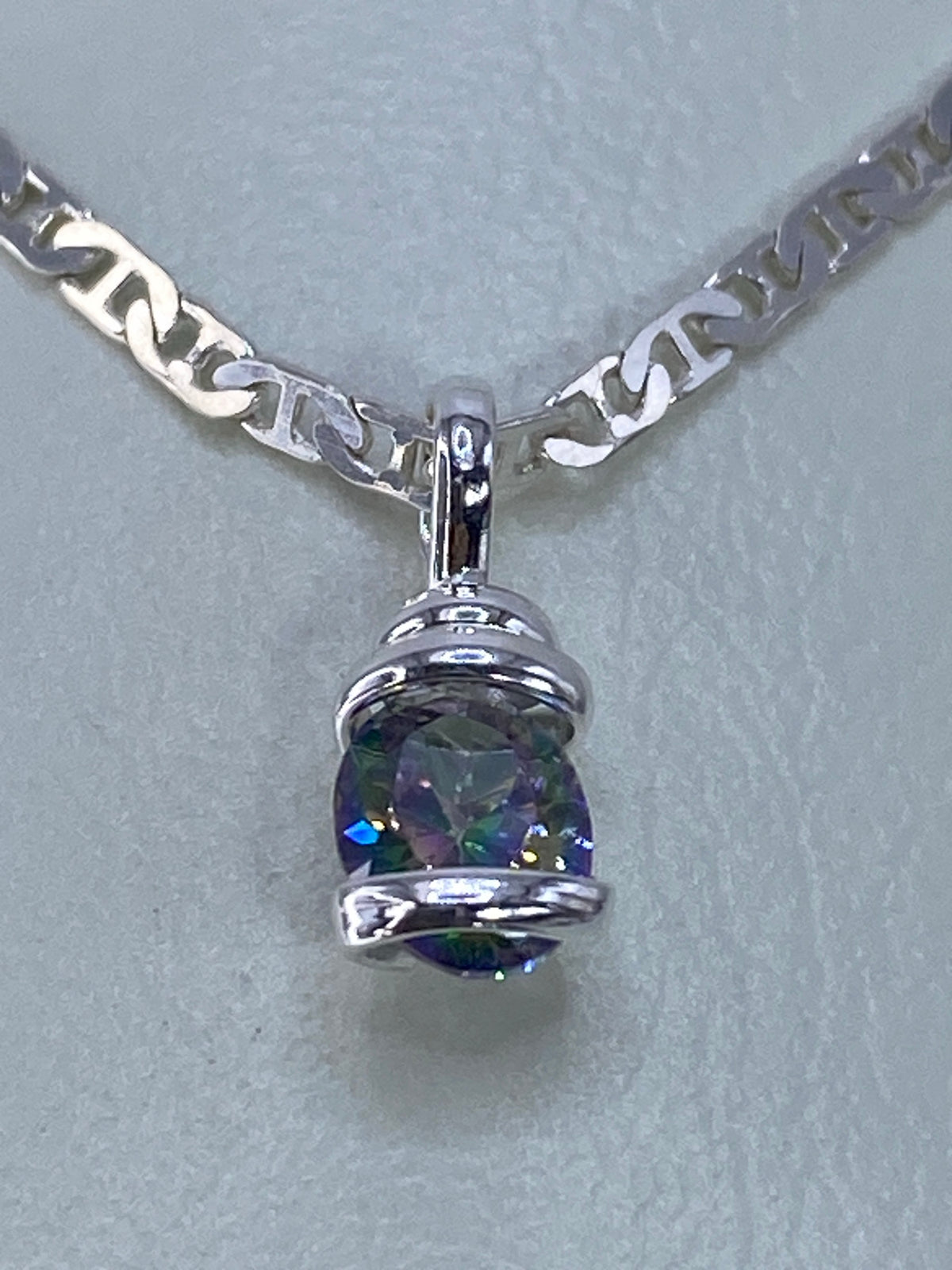 Detalle del dije de plata mostrando la circonia con destellos en azul, verde, amarillo y púrpura