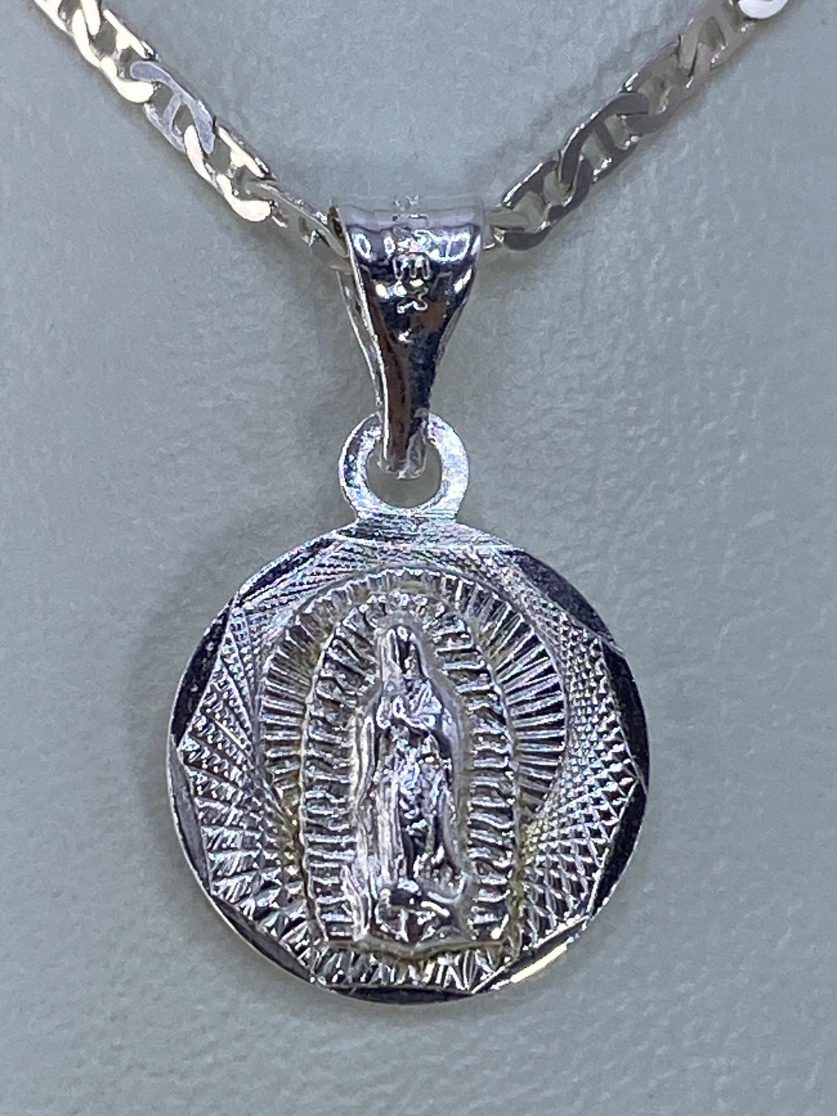 Dije de plata 925 con la Virgen de Guadalupe en relieve, visto de frente mostrando la aureola radiante