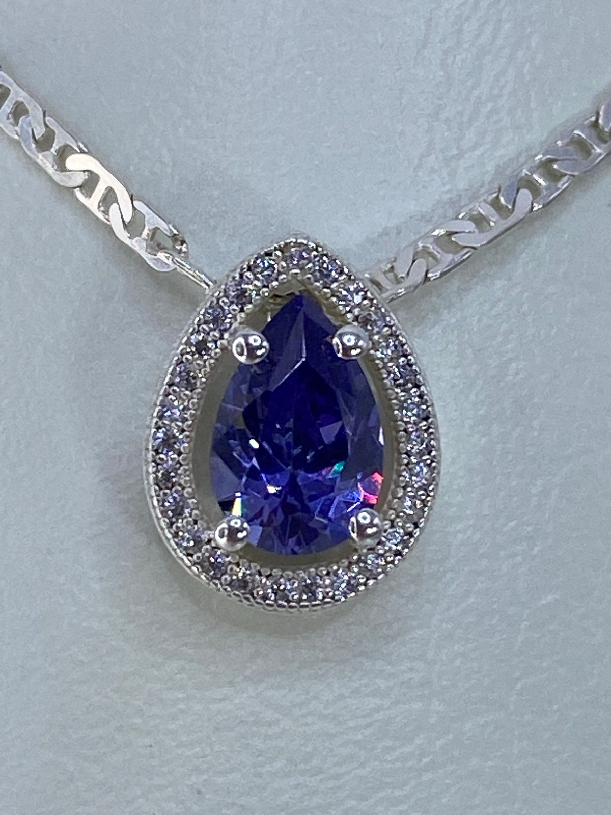 Dije de plata con circonia azul facetada sobre fondo gris claro