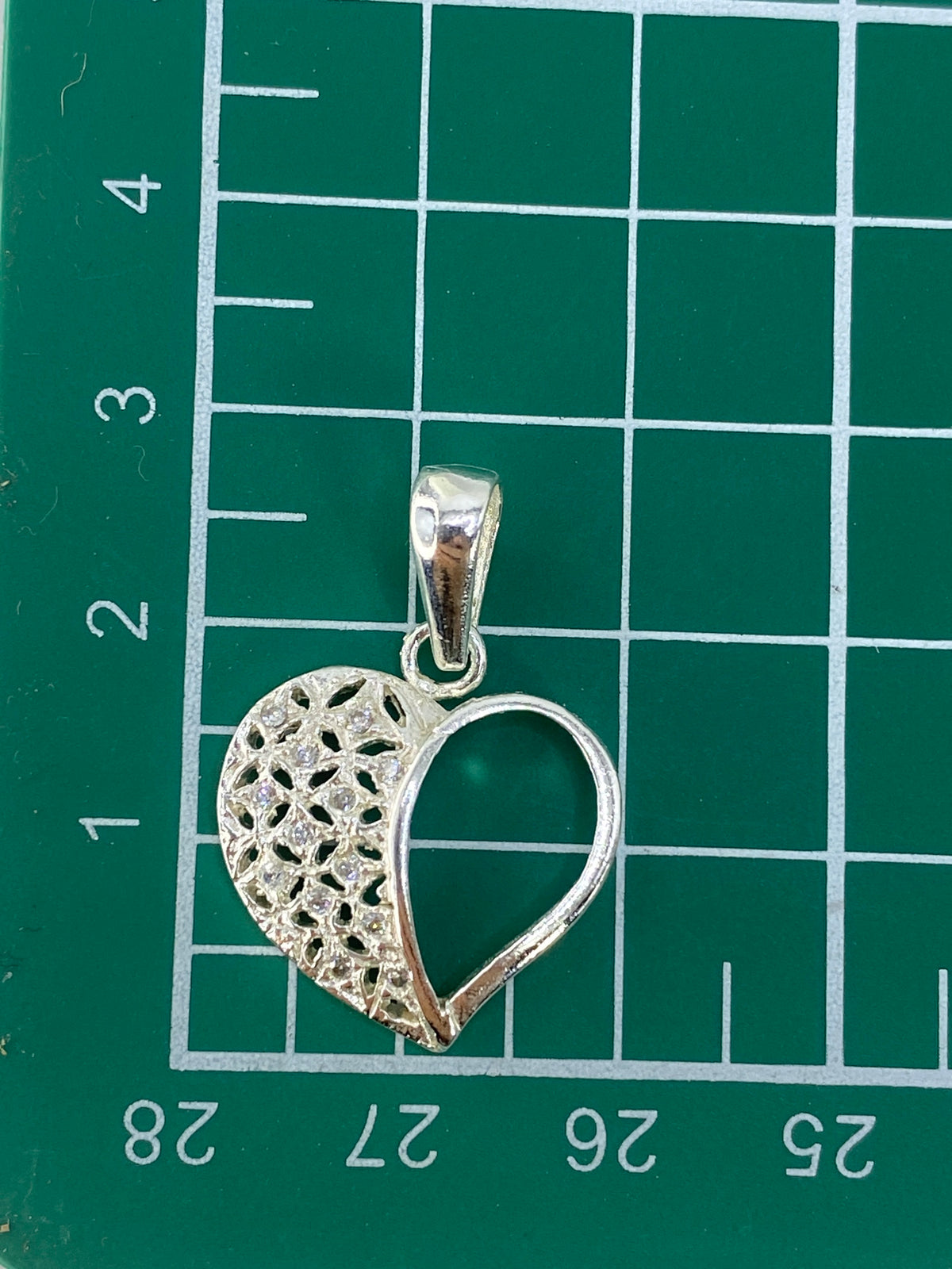 Dije corazón sobre escala de centímetros mostrando tamaño real 2.8 cm