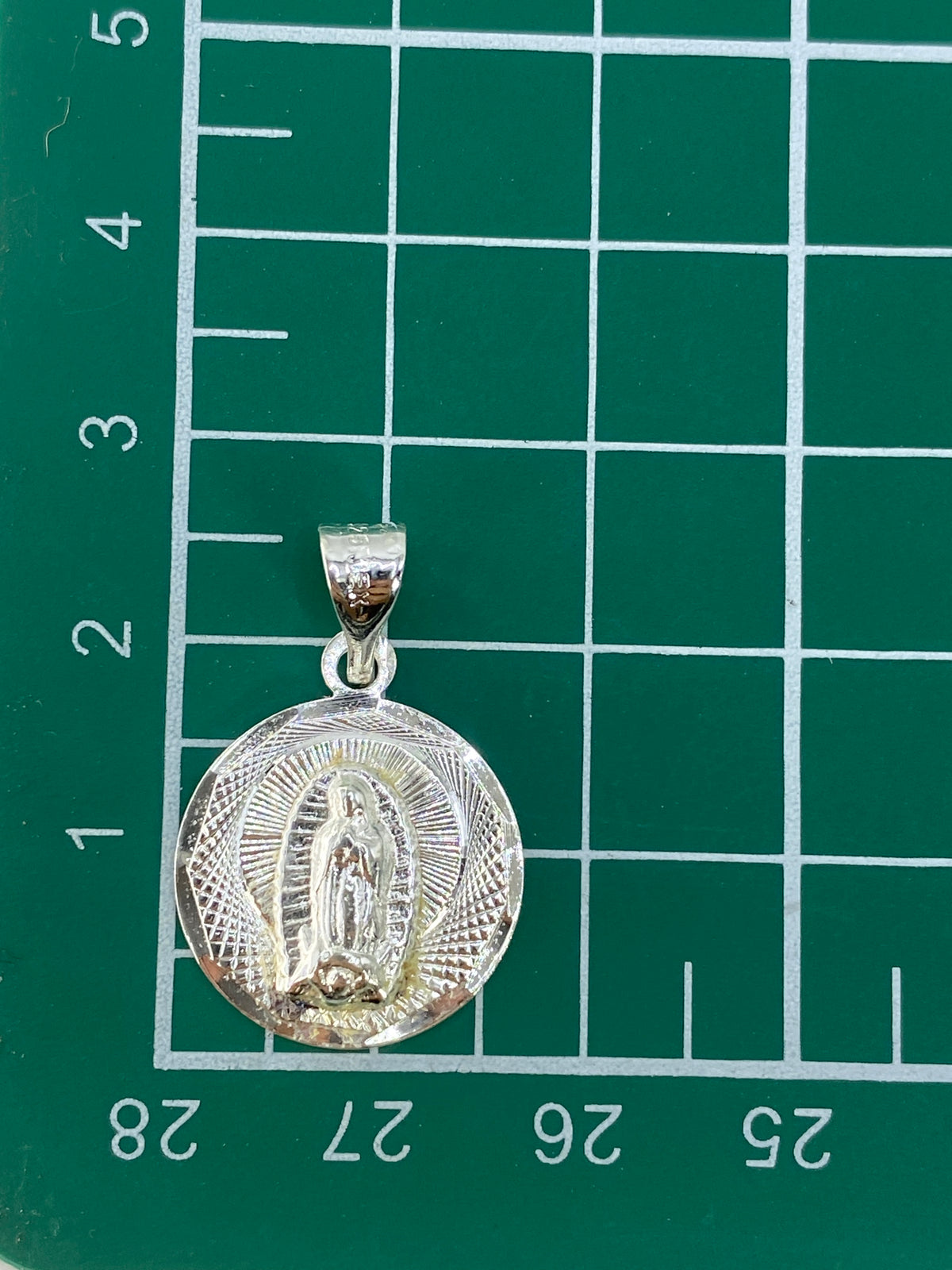 Dije de 2.5 cm sobre escala de medición con Quinto 925 visible