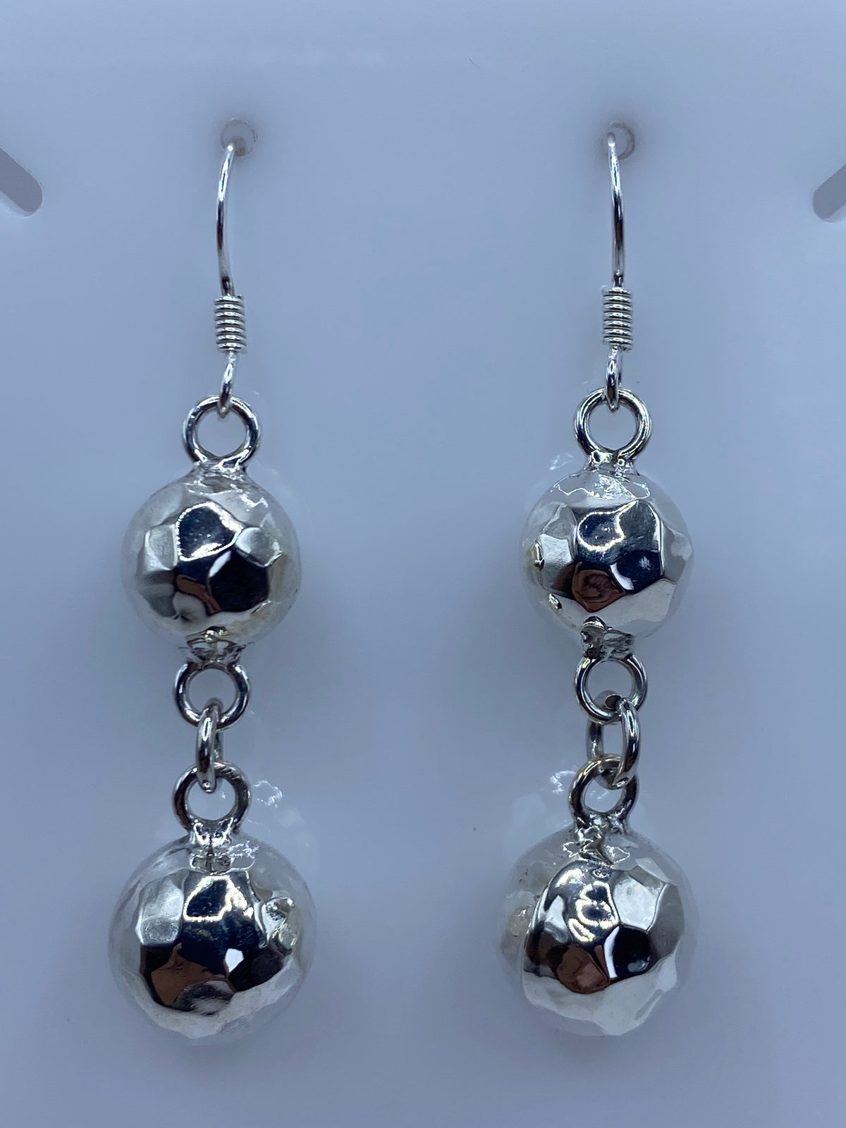 Par de aretes de plata con esferas facetadas repujadas a mano, colgando de ganchos de plata pulida