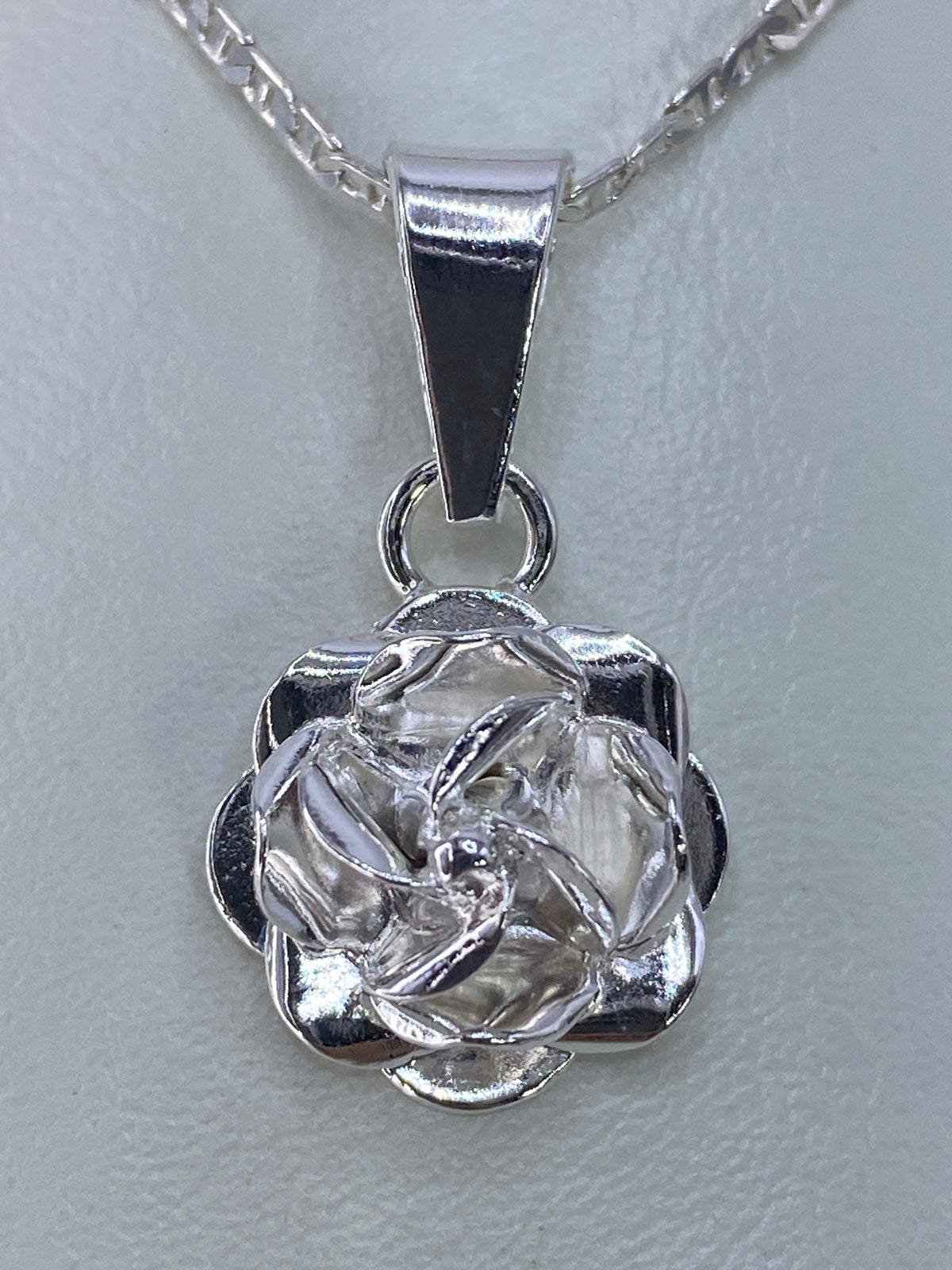 Dije floral de plata repujado en relieve, colgante sobre cadena plateada