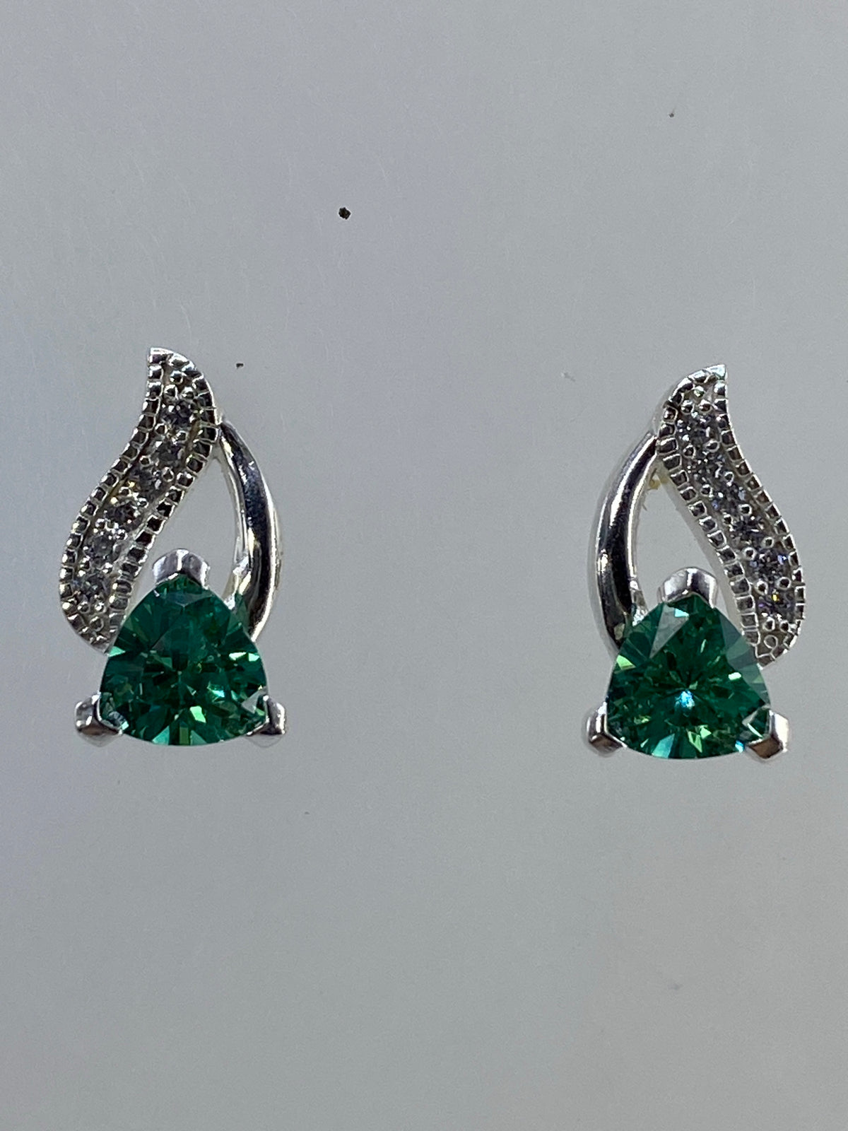Par de aretes de plata 925 con alas de ángel y circonia verde esmeralda sobre fondo neutro