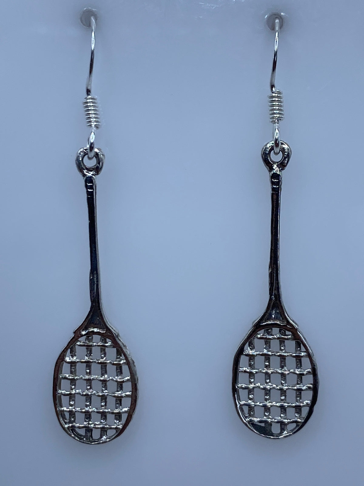 Aretes de plata calado con diseño de raquetas en par, colgando sobre fondo blanco