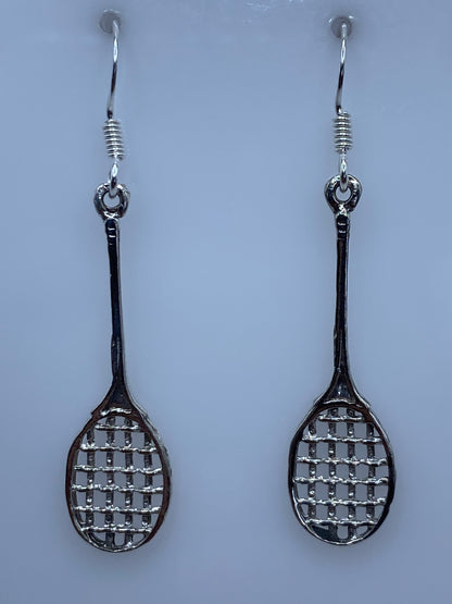 Aretes de plata calado con diseño de raquetas en par, colgando sobre fondo blanco