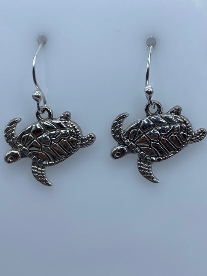 Aretes de tortuga marina colgados de ganchos de plata, mostrando el tamaño proporcional