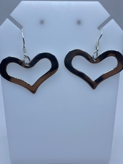 Par de aretes de plata con forma de corazón calado, colgando de ganchos de plata en pieza de exhibición blanca