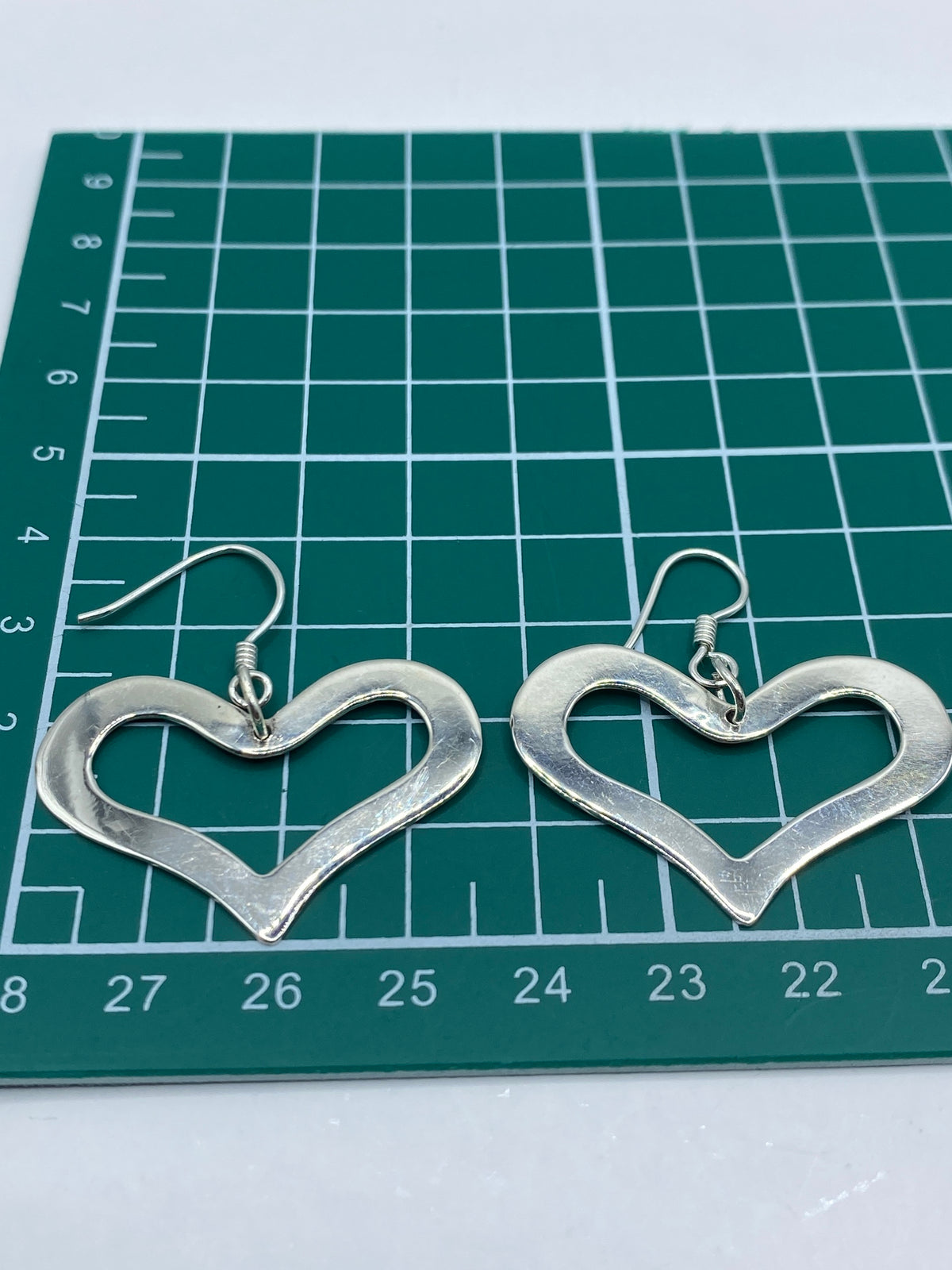 Aretes corazón de plata sobre fondo neutro, piezas caladas hecho a mano en Taxco