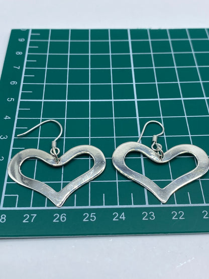 Aretes corazón de plata sobre fondo neutro, piezas caladas hecho a mano en Taxco