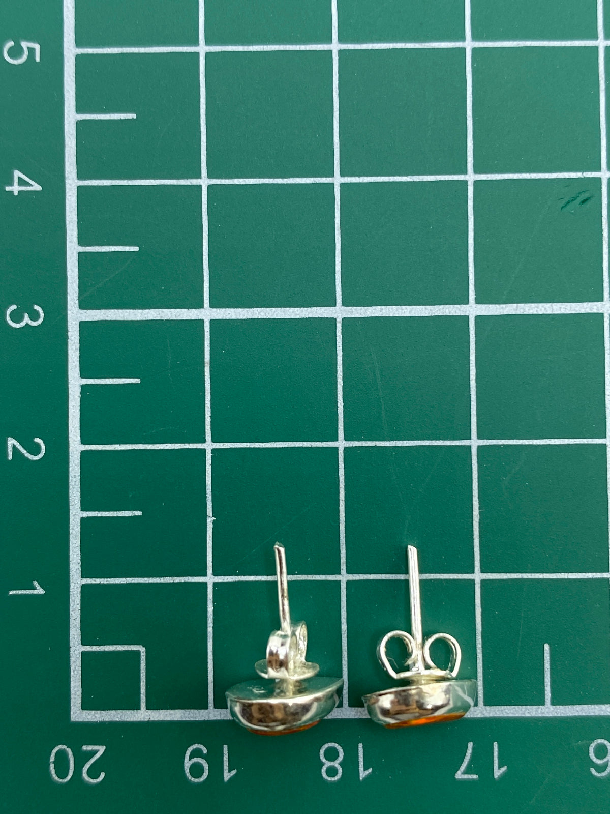 Aretes con ópalo de fuego multicolor sobre fondo gris, mostrando el acabado pulido de la plata